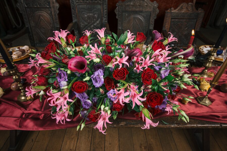 top table centre piece jewel tones big colourful roses peace lilies red purple pink
